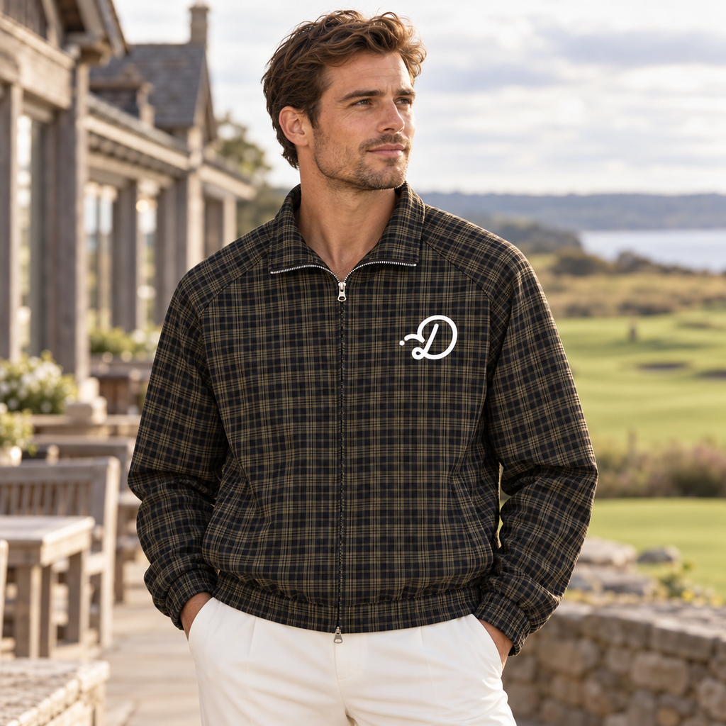 Man wearing the Duffed Links Plaid Track Jacket outside a coastal golf clubhouse, showing the white D chest logo